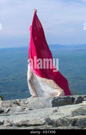 Female dancer in white dress wrapped in red fabric blowing in the wind on summit of Mt. Kearsarge, NH. Stock Photo