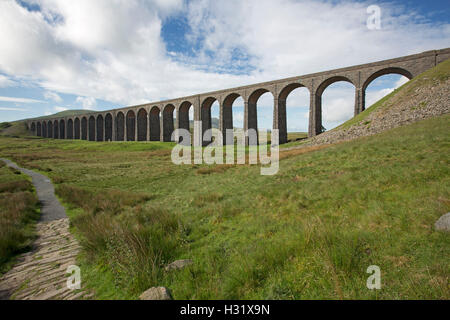 Historic Ripplehead viaduct stretching across valley of Yorkshire moors & beside narrow walking track under blue sky England Stock Photo