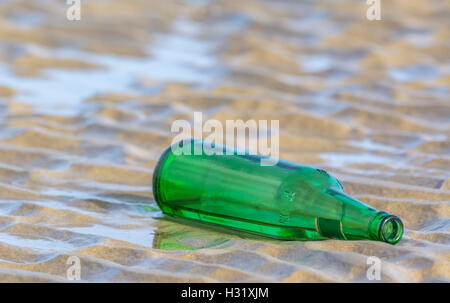 Discarded empty green bottle left on a sandy beach. Stock Photo