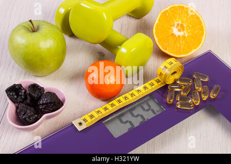 Tape measure on digital bathroom scale for weight of human body, dumbbells for fitness, fresh fruits and tablets supplements, Stock Photo