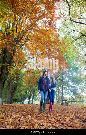 Young couple enjoying a walk together in Autumn. They are hand in hand and talking as they stroll through the park. Stock Photo