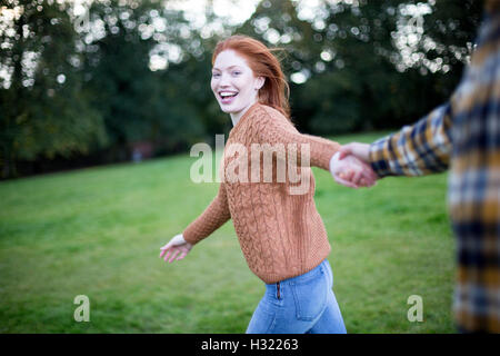 Point of view shot of a young woman running whilst holding her partners hand. She is looking at the camera. Stock Photo