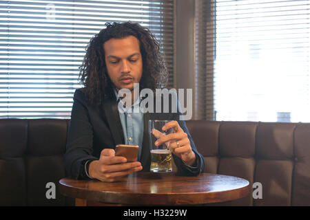 Young man using his smartphone whilst enjoying a beer in a bar. Stock Photo