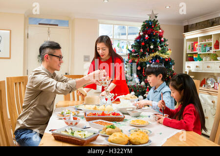 Chinese family enjoying their christmas dinner. They are eating traditional Chinese food. The parents are serving it round the t Stock Photo