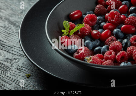 black plate with fresh healthy berries and mint on a dark background Stock Photo