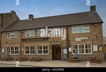 Wheatsheaf hotel, old brown stone building in English village of Bakewell with man sitting at outside table under blue sky Stock Photo