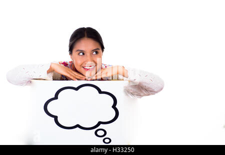 Charming young woman wearing traditional andean blouse with colorful embroideries, matching necklace and earrings, facing camera while posing, leaning over sign which has conversation bubble drawn on it, white studio background Stock Photo