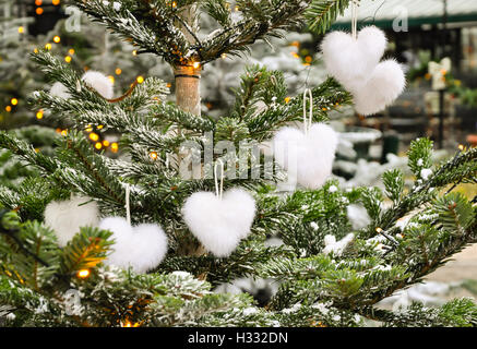 Unusual creative romantic Christmas or New Year decoration -white fluffy heart shape christmas toys on spruce in winter. Stock Photo