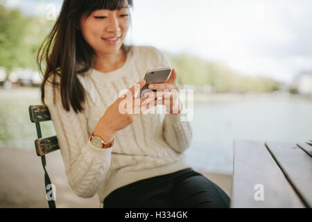 Shot of happy young female using mobile phone at outdoor cafe. Young female sitting at table reading text message on her cellpho Stock Photo