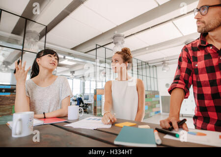 Group of multiracial coworkers discussing new business ideas around a table in creative office. Stock Photo
