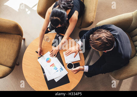 Overhead view of young businessman and woman working on graphs while sitting at office lobby. Corporate people discussing new bu Stock Photo