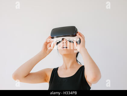 Asian woman using the virtual reality headset and looking away. Female wearing VR goggles against grey background. Stock Photo