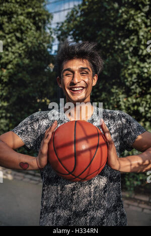 Portrait of smiling young man passing basketball. Teenage guy looking at camera with a ball in hands on outdoor court. Stock Photo