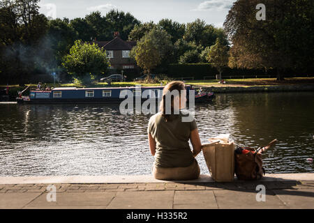 A young woman sitting on the banks of the River Thames in Kingston-Upon-Thames, Surrey, England, UK Stock Photo