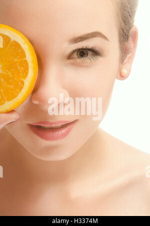 Face of a beautiful young woman who is holding a half of orange slices in front of his eyes and smiling. White background Stock Photo