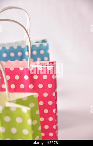 Detail of three paper bags to buy colored with white circles in a row on white table isolated. Front elevated view Stock Photo