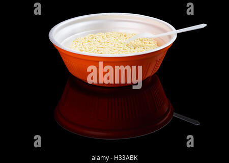 Instant noodles in red plastic plate with one plastic fork isolated on black reflecting background Stock Photo