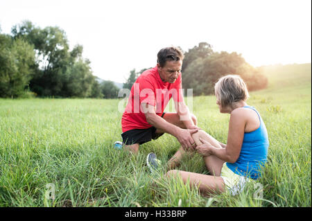 Senior runners in green field. Woman with injured knee. Stock Photo