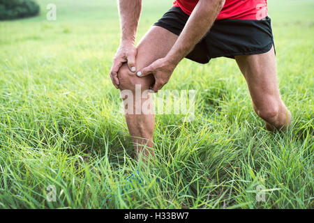 Unrecognizable runner in green field. Man with injured knee. Stock Photo