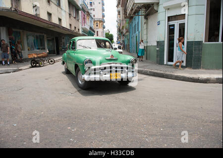 HAVANA - JUNE 15, 2011: Cubans talk on the corner as a vintage American car serving as taxi drives past in a typical scene. Stock Photo