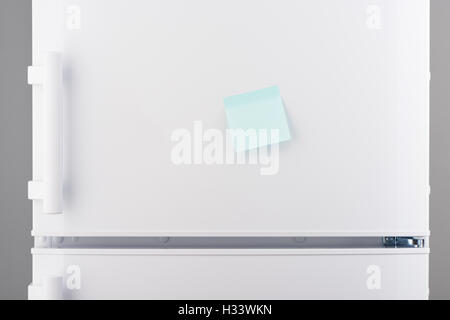 Blank light blue sticky paper note on white refrigerator door Stock Photo
