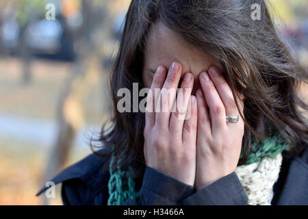 Girl with dark hair covers face  her hands Stock Photo