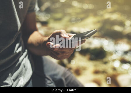 Male tourist using mobile smart phone for GPS navigation in outdoors nature on bright sunny day Stock Photo