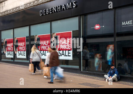 Out of focus blurred shoppers, people walking figures passing Half Price Autumn Sale signs at Debenhams Store, Manchester, UK. Sale and reductions, deals & offers, clearance items, discount, price, promotion, retail business at Debenhams department store. Stock Photo