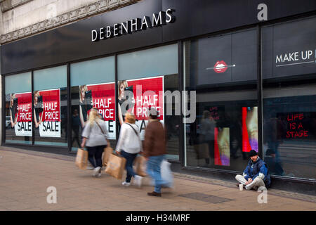 Out of focus blurred shoppers, people walking figures passing Half Price Autumn Sale signs at Debenhams Store, Manchester, UK. Sale and reductions, deals & offers, clearance items, discount, price, promotion, retail business at Debenhams department store. Stock Photo
