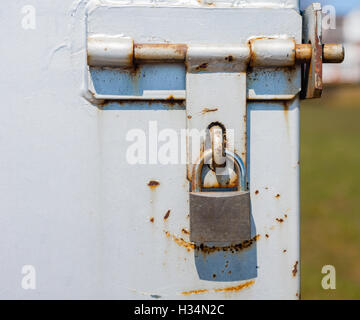 Partly rusted closed padlock in scratched metal latch with blurred background on right. Stock Photo