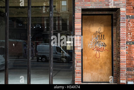 View of a vacant shop / store with boarded up door, with graffiti on it saying "I will miss you" Stock Photo