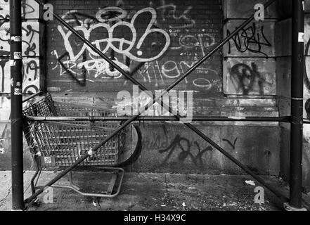 Monochrome gritty image of scaffolding crossed poles with abandoned shopping trolley and a graffiti covered wall in New York