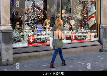 People passing shop windows of business retail fashion stores in the city centre. Liverpool, Merseyside, UK. 5th October, 2016.  Rapid Discount Outlet store in Williamson Square are celebrating early this year with a full-on decorated Christmas window featuring a huge Christmas tree, dozens of lights, hanging snowflakes and a Father Christmas! Liverpool's business district, Stock Photo
