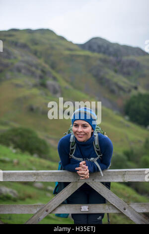 A woman rests on a gate in the Great Langdale valley in The Lake District, Cumbria, England, UK Stock Photo