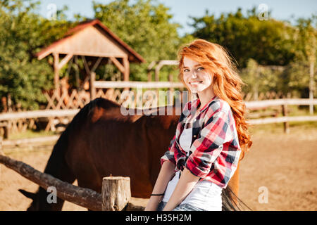 Portrait of cheerful attractive young woman cowgirl with horse in village Stock Photo