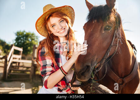 Portrait of happy redhead young woman cowgirl in hat with her horse Stock Photo