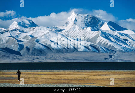 In  early  morning  light  a  western  visitor  walks  towards  Lake  Manasarovar  and  on  its  southern  shore  rises  Gurla Stock Photo