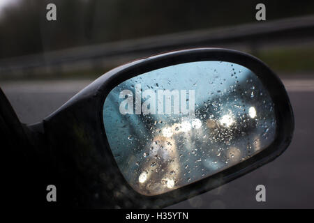 Looking at a rain covered car wing mirror with refelctions of car headlights. Stock Photo