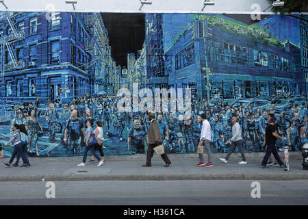 NYC pedestrians walk past a large mural painted by Logan Hicks on the Bowery Mural Wall, Houston Street Stock Photo