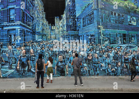 NYC pedestrians walk past a large mural painted by Logan Hicks on the Bowery Mural Wall, Houston Street Stock Photo