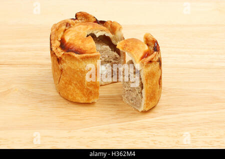 Handmade hot water crust pork pie with a slice cut out on a wooden chopping board Stock Photo