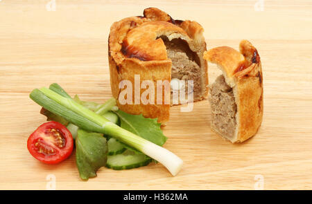 Handmade hot water crust pork pie with salad on a wooden chopping board Stock Photo