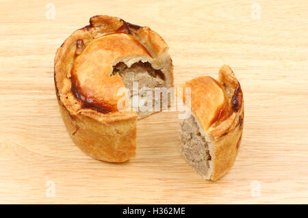 Handmade hot water pastry pork pie with a slive cut out on a wooden chopping board Stock Photo