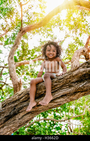 Three years old child sitting on a tree brunch in the jungle forest having fun outdoors Stock Photo