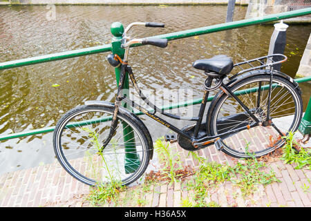 Old bicycle parked by railing on quayside of canal - weed and cigarette butts on the street in downtown Leiden, Netherlands Stock Photo