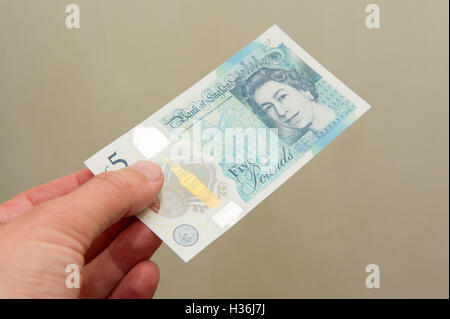 Man handing over a new plastic (polymer) five pound note Stock Photo