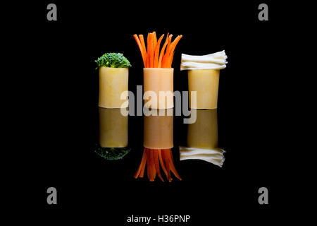 Three pieces of pasta with embedded red carrots, green broccoli and white cheese on a black reflection background