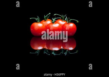 Five isolated tomatoes on a black shiny background Stock Photo