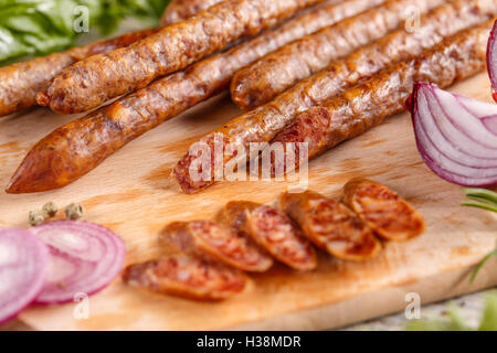 Smoked thin sausage salami slices on wooden cutting board Stock Photo