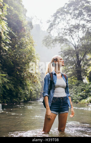 Shot young woman standing in water of mountain stream. Female hiker crossing the forest creek. Stock Photo